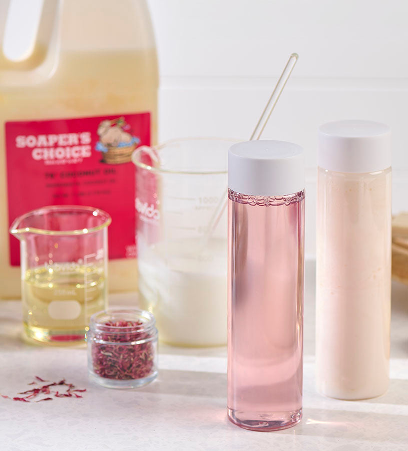 A variety dark and clear bottles with oils, a wood spoon, two brushes, and a bar of soap